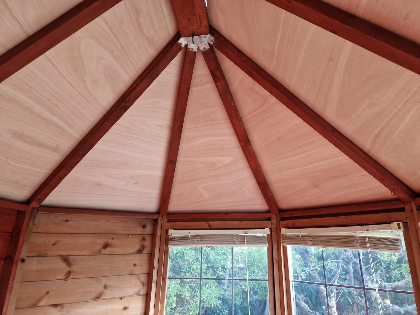 Interior view of a wooden structure with a hexagonal ceiling and natural light coming through windows.